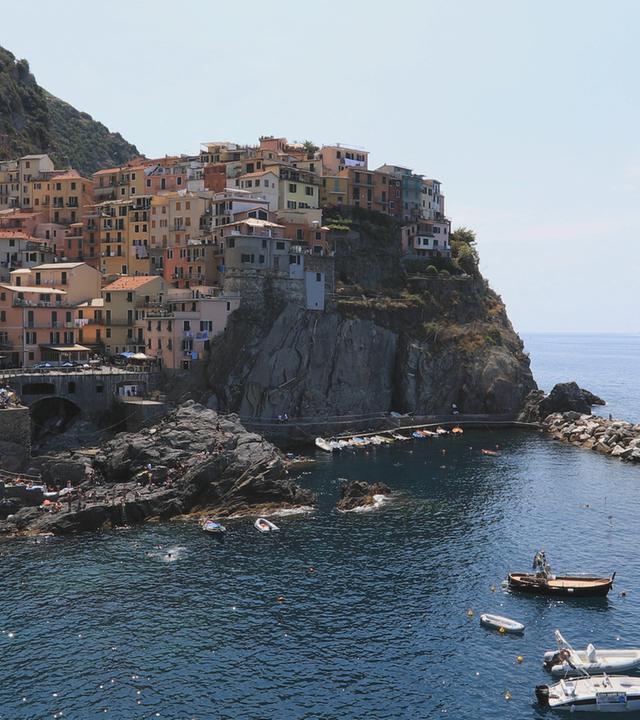 "Die Italienische Riviera": Ein Bergdorf der Cinque Terre mit Meer und Booten im Vordergrund.