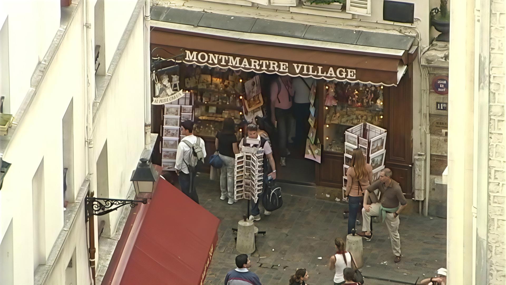 „Montmartre – die Seele von Paris“: Souvenirshop mit der Aufschrift „Montmartre Village“. Davor einige Touristen.