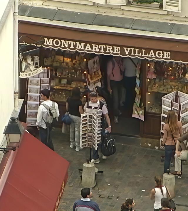 „Montmartre – die Seele von Paris“: Souvenirshop mit der Aufschrift „Montmartre Village“. Davor einige Touristen.