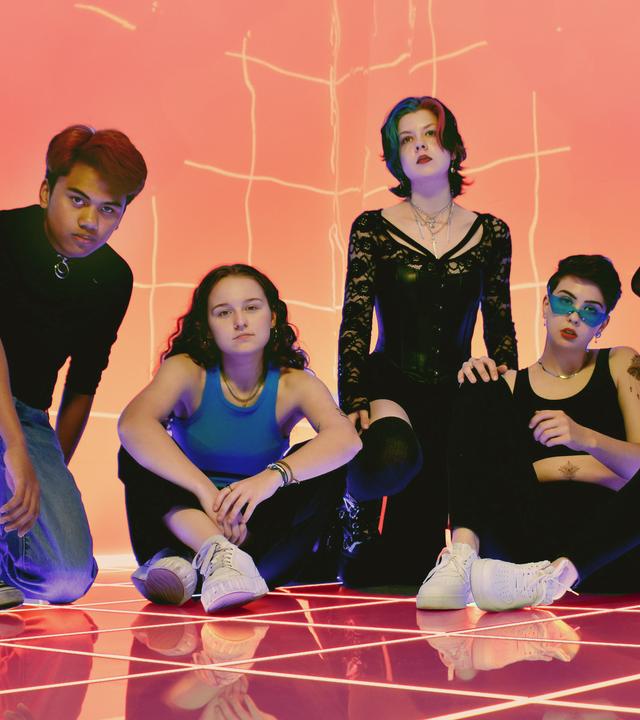 Fünf junge Menschen posieren für ein orangefarbenen Hintergrund mit Streifen.