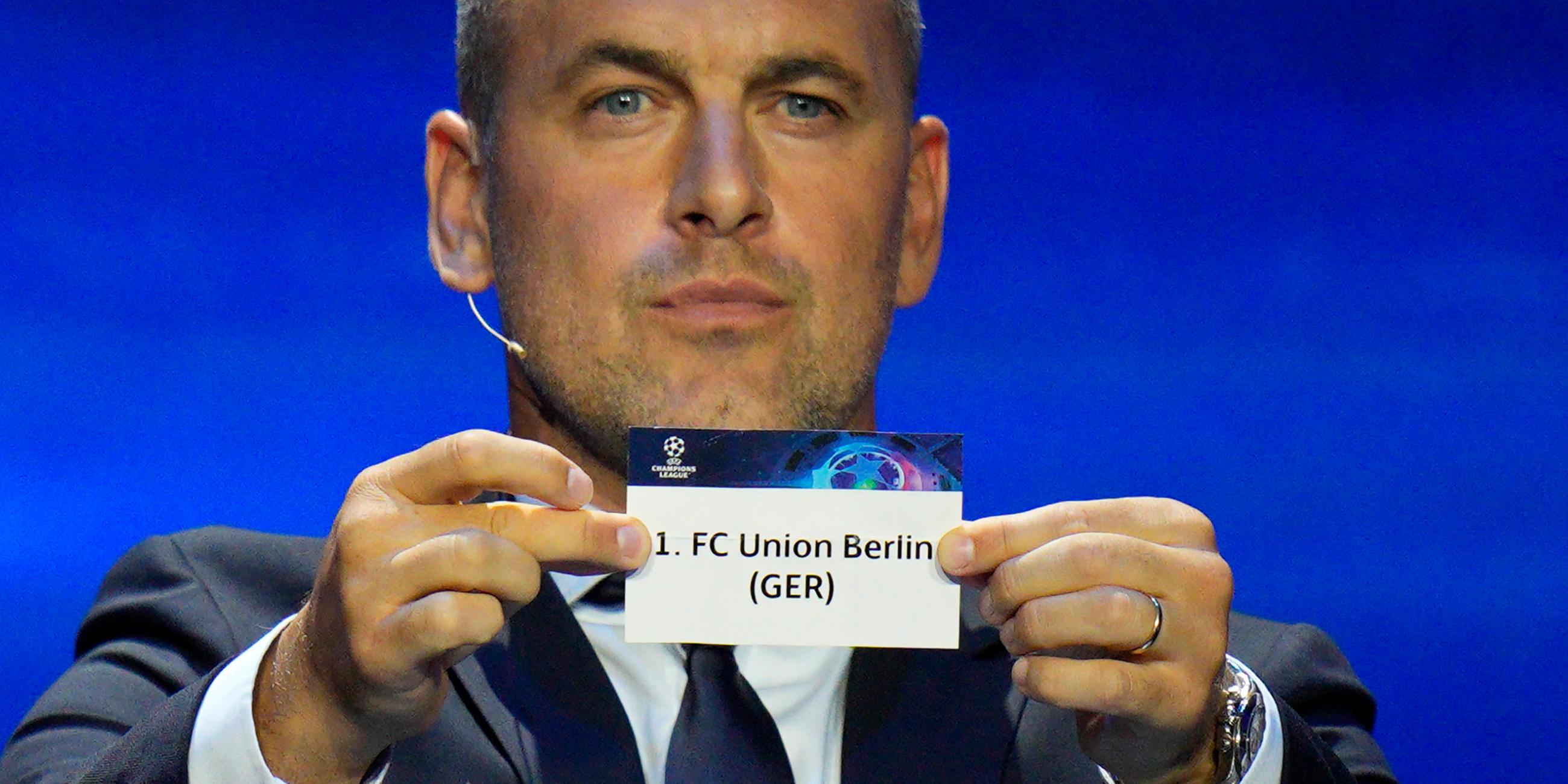 Der ehemalige Fußballstar Joe Cole zeigt ein Ticket des Fußballvereins 1. FC Union Berlin während der Auslosung der Gruppenphase der UEFA Champions League 2023/24.