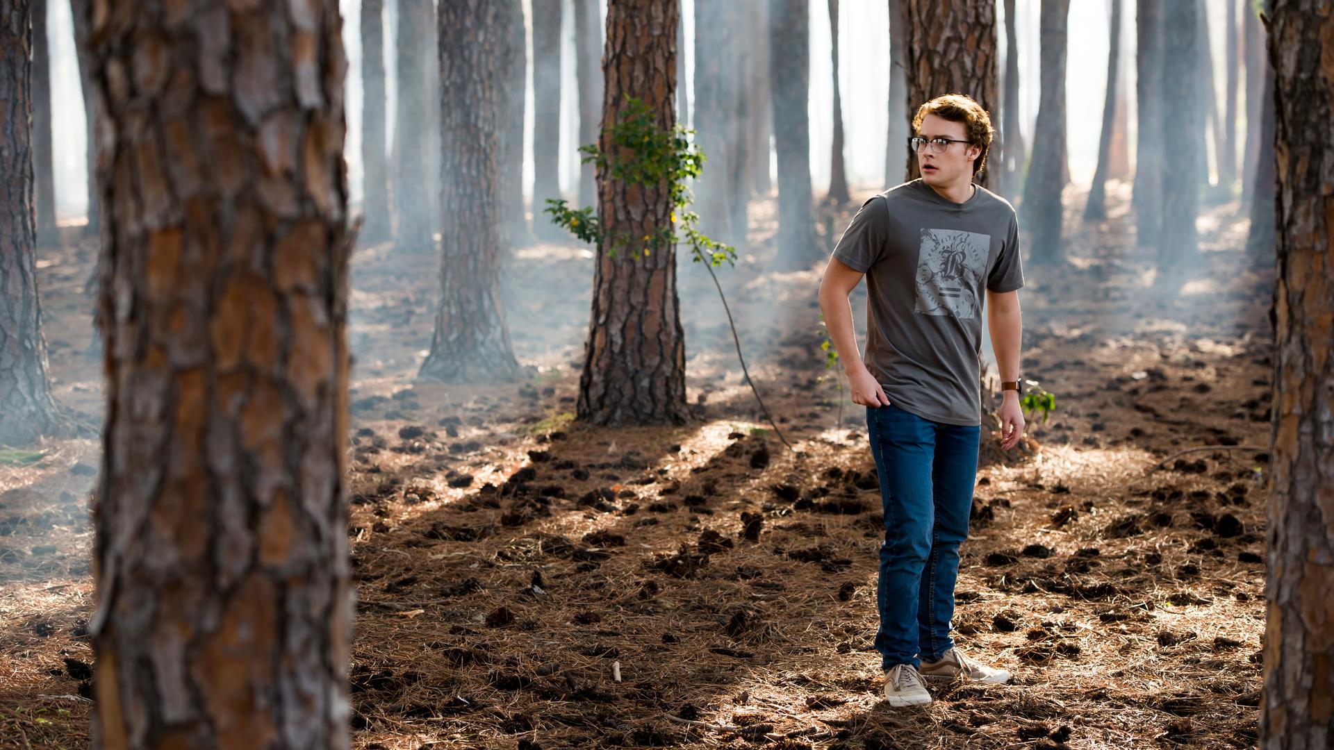 Peter steht inmitten von kahlen Bäumen im Wald.