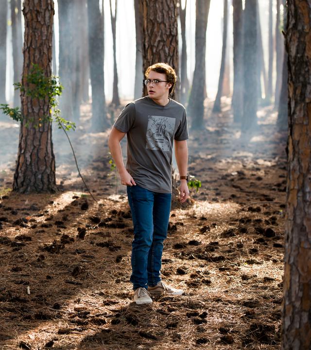 Peter steht inmitten von kahlen Bäumen im Wald.