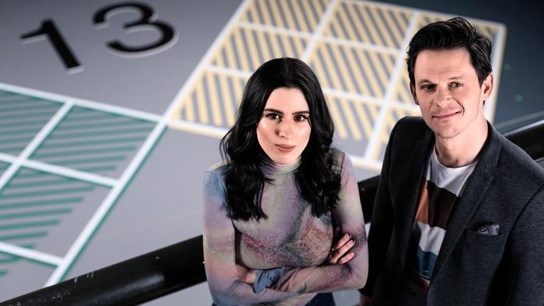 "13 FRAGEN": Salwa Houmsi und Jo Schück stehen oberhalb des Spielfeldes.