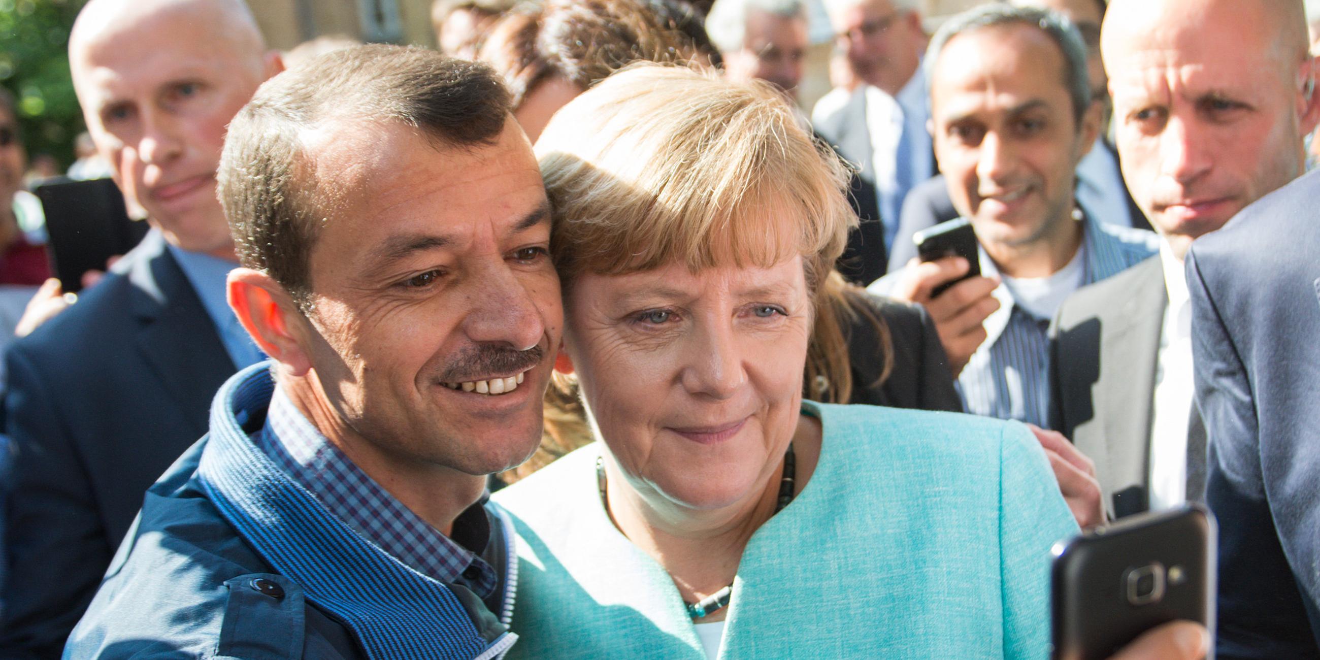 Das Bild zeigt Angela Merkel wie sie mit einem Flüchtling ein Selfie macht.