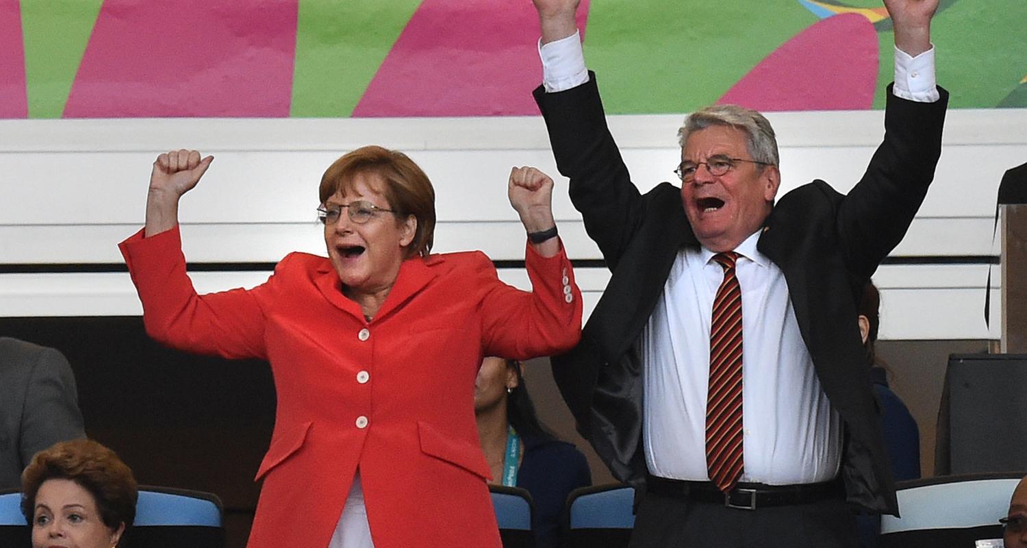 Das Bild zeigt Angela Merkel und den damaligen Bundespräsidenten Joachim Gauck jubelnd bei einem Fußballspiel.