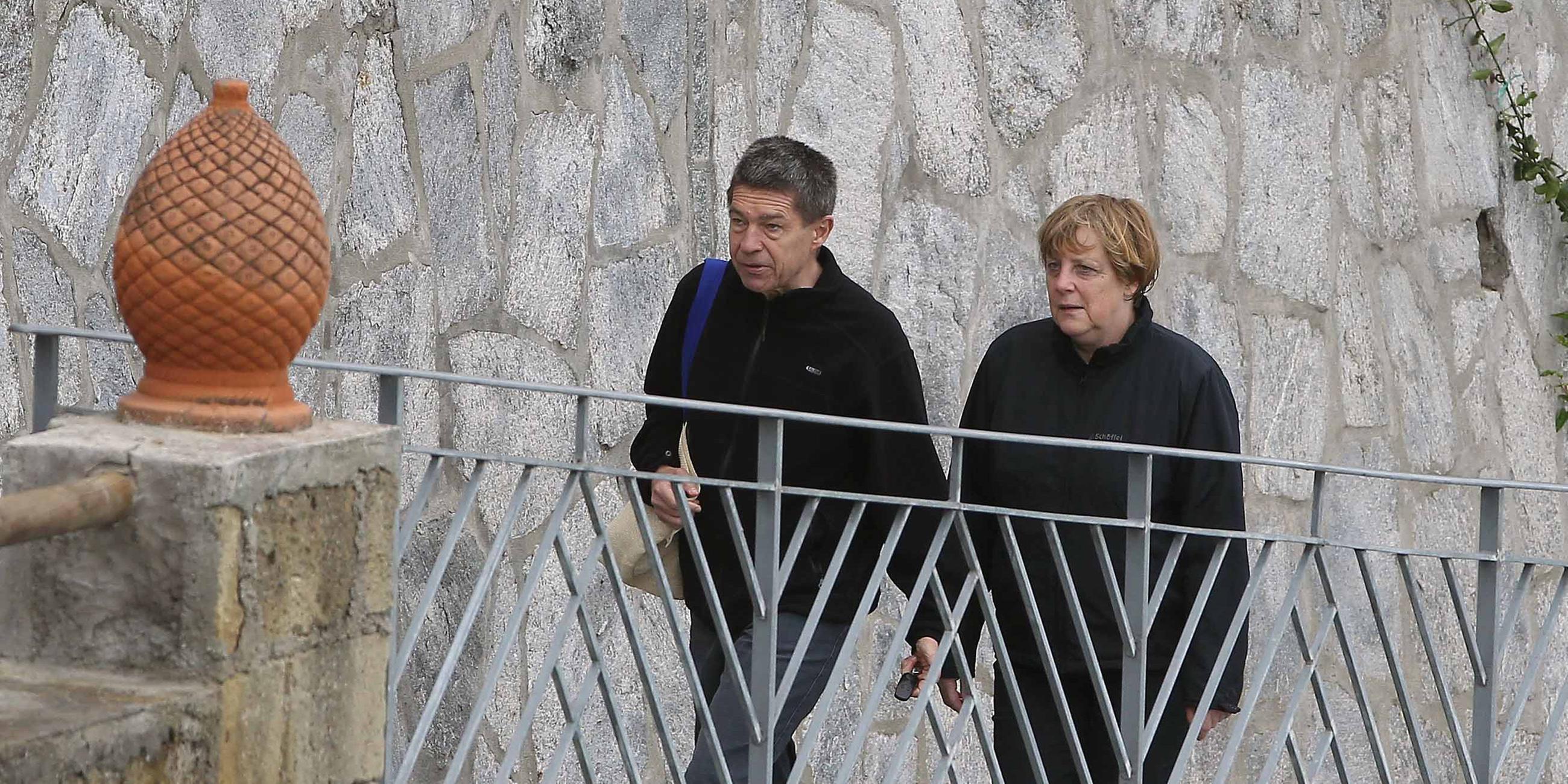 Das Bild zeigt Angela Merkel und ihren Ehemann Joachim Sauer vor einer Mauer.