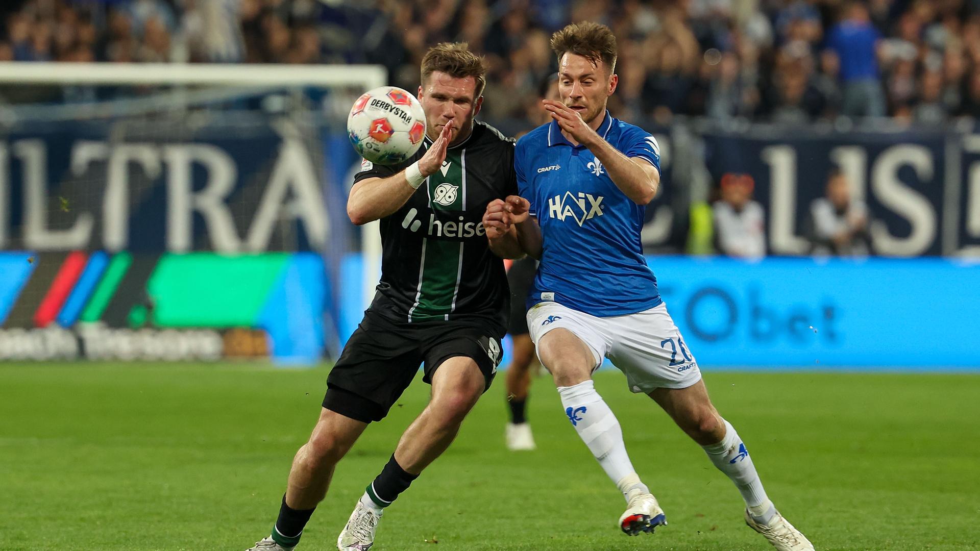 Benjamin Kaellman (Hannover 96) und Matthias Bader (SV Darmstadt 98) im Zweikampf am 11.04.2026 in Darmstadt.
