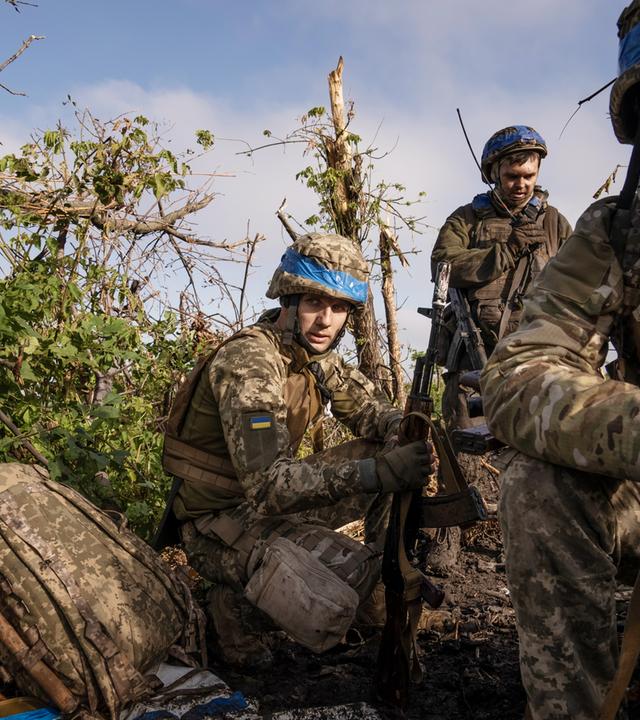 Soldaten in Camouflage kauern zwischen Büschen und Gestrüpp.