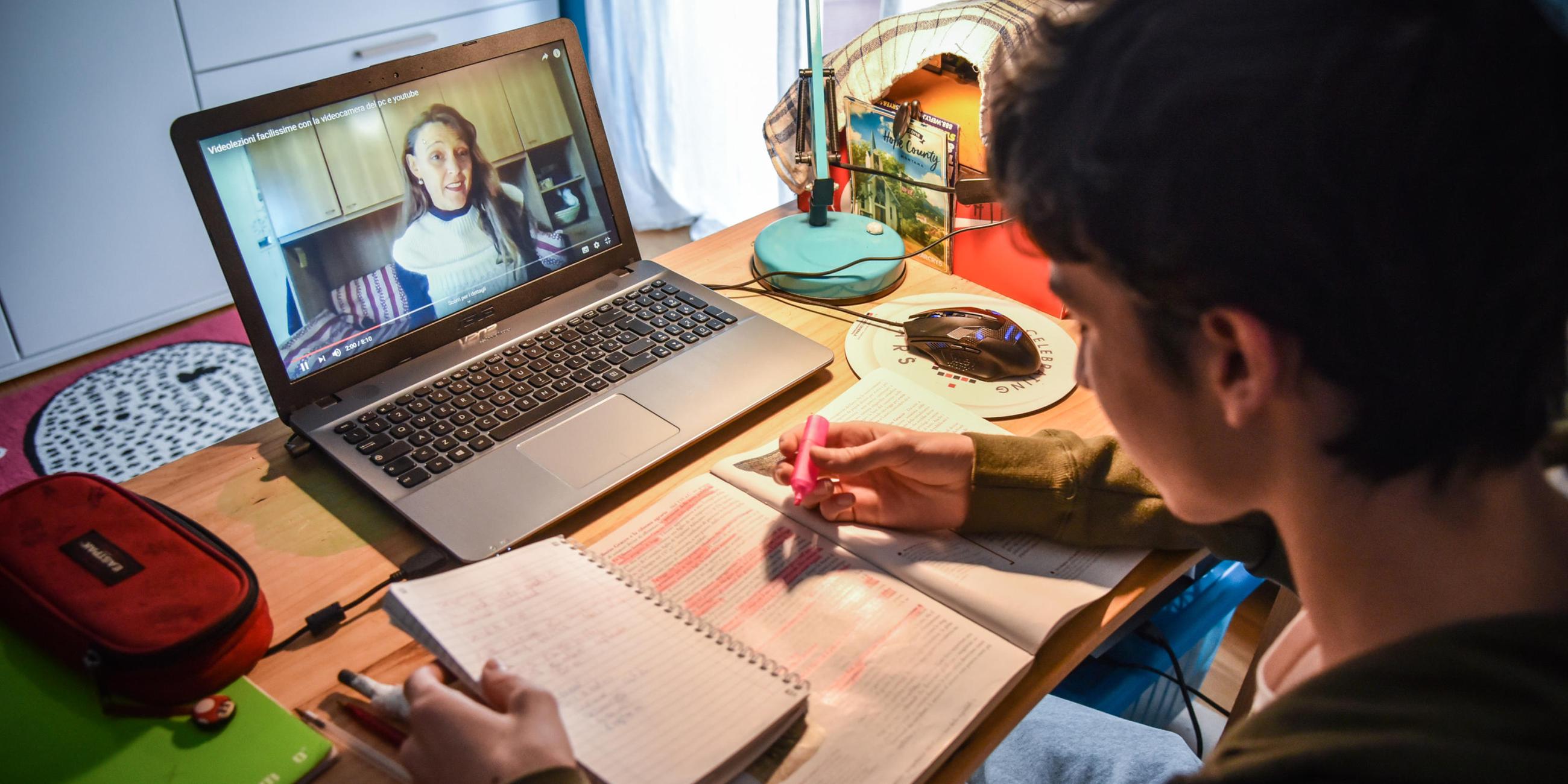 Ein Schüler sitzt vor einem Laptop und macht arbeit online an Schul-Aufgaben