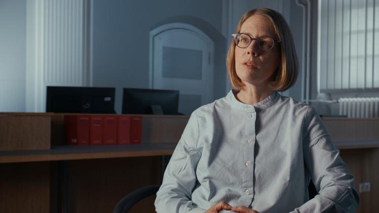 "Systemfehler: Der Cum-Ex Skandal": Staatsanwältin Anne Brorhilker sitzt in einem Gerichtssaal und schaut an der Kamera vorbei. Im Hintergrund steht die Richterbank.