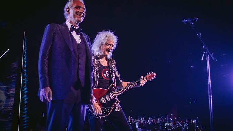 "Andrea Bocelli: Sommernacht in der Toskana": Andrea Bocelli und Brian May stehen nebeneinander auf einer Bühne. Brian May hält eine Gitarre.