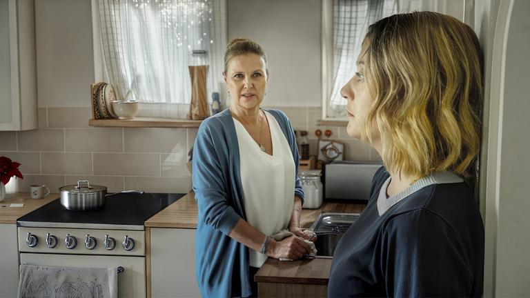 "Das gläserne Kind": In der Küche stehen Anne Schuchardt (Katharina Böhm) und Helen Schuchardt (Hanna Plaß), die sich miteinander unterhalten. Helen steht mit dem Rücken an die Wand gelehnt und schaut ausdruckslos nach vorne. Ihre Mutter Anne steht an der Küchenzeile und sieht sie an.