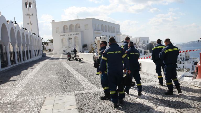 "Santorini – Tanz auf dem Vulkan": Mehrere Feuerwehrleute, die nur von hinten zu sehen sind, laufen über eine Straße. Neben ihnen ist Absperrband zu sehen.