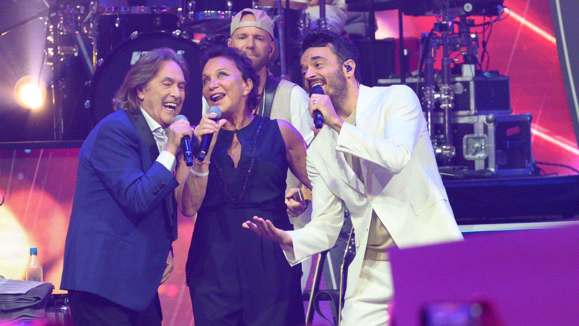 "Die Giovanni Zarrella Show": Ricchi E Poveri und Giovanni Zarrella bei einem gemeinsamen Auftritt. Die drei vermitteln Ausgelassenheit, während sie in ihre Mikrofone singen. Im Hintergrund spielt der Gitarrist der Zarrella-Band.