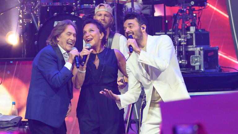 "Die Giovanni Zarrella Show": Ricchi E Poveri und Giovanni Zarrella bei einem gemeinsamen Auftritt. Die drei vermitteln Ausgelassenheit, während sie in ihre Mikrofone singen. Im Hintergrund spielt der Gitarrist der Zarrella-Band.