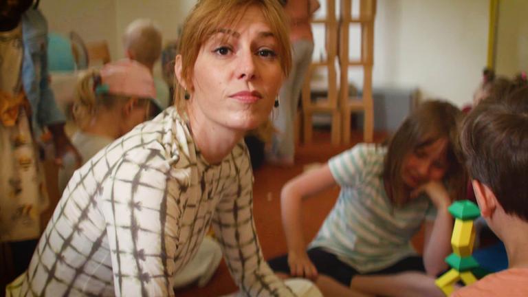 "Am Puls mit Eva Schulz": Eva Schulz sitzt in der Kita St. Lukas in Salzgitter auf dem Boden. Neben ihr spielen Kinder mit Bauklötzen, im Hintergrund befinden sich in der Unschärfe weitere Kinder.
