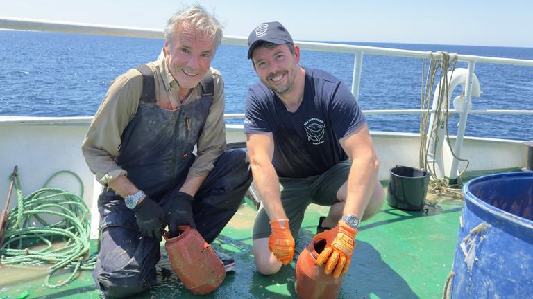 "Hannes Jaenicke im Einsatz für den Oktopus:" Hannes Jaenicke und Peter Hammarstedt, dem weltweiten Kampagnenleiter von Sea Shepherd mit illegalen Oktopus-Fangtöpfen in Griechenland, beide knieend auf dem Schiff.