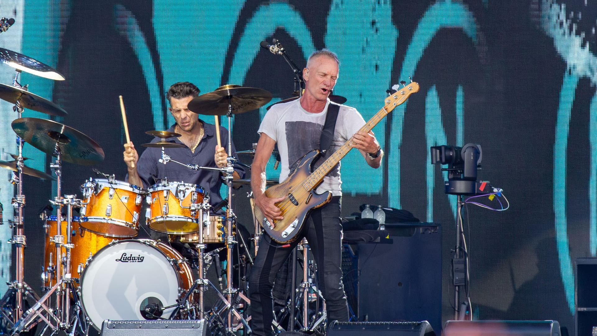 "Isle of Wight Festival 2025": Sting wärend eines Auftritts auf der Bühne. Er spielt eine Bassgitarre. Im Hintergrund ein Musiker an einem Schlagzeug.