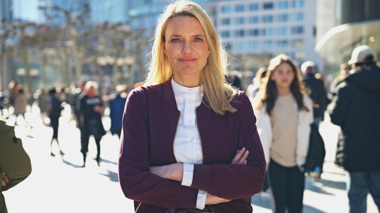 "Am Puls mit Sarah Tacke: Flucht und Krise - 10 Jahre "Wir schaffen das": Sarah Tacke steht in der belebten Fußgängerzone in Frankfurt und schaut in die kamera.