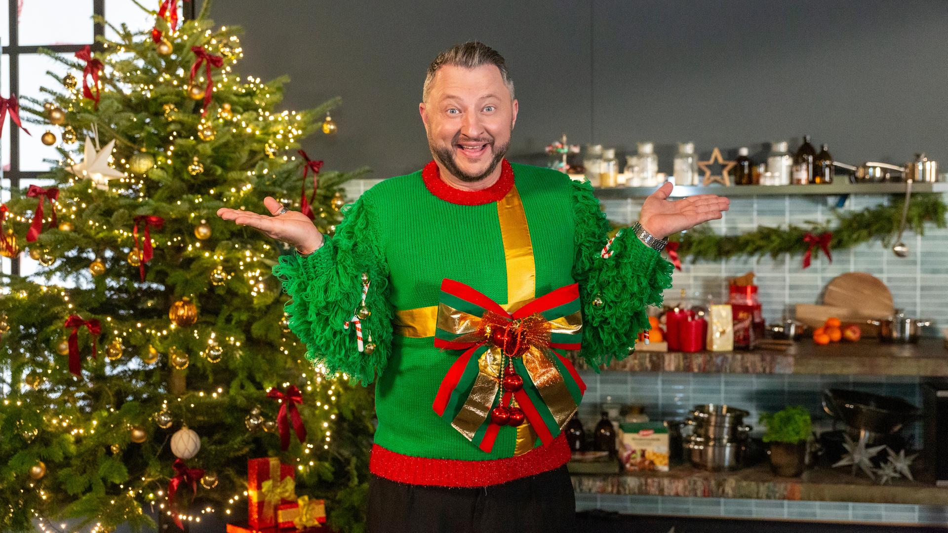 "besseresser: Die Tricks in Weihnachtsprodukten": Sebastian Lege trägt einen Weihnachtspulli mit großer Schleife und steht vor einem Weihnachtsbaum.