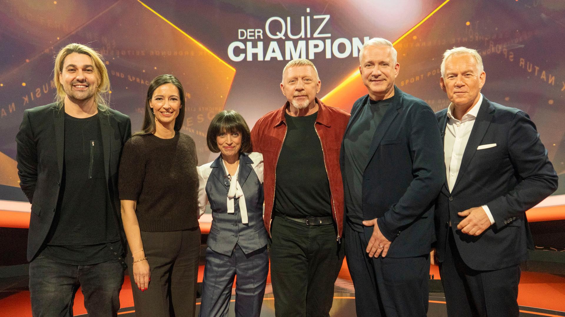 "Der Quiz-Champion": Gruppenbild: David Garrett, Pinar Atalay, Anna Thalbach, Boris Becker, Alexander Herrmann und Johannes B. Kerner stehen im Studio vor dem Sendungslogo und lächeln in die Kamera.