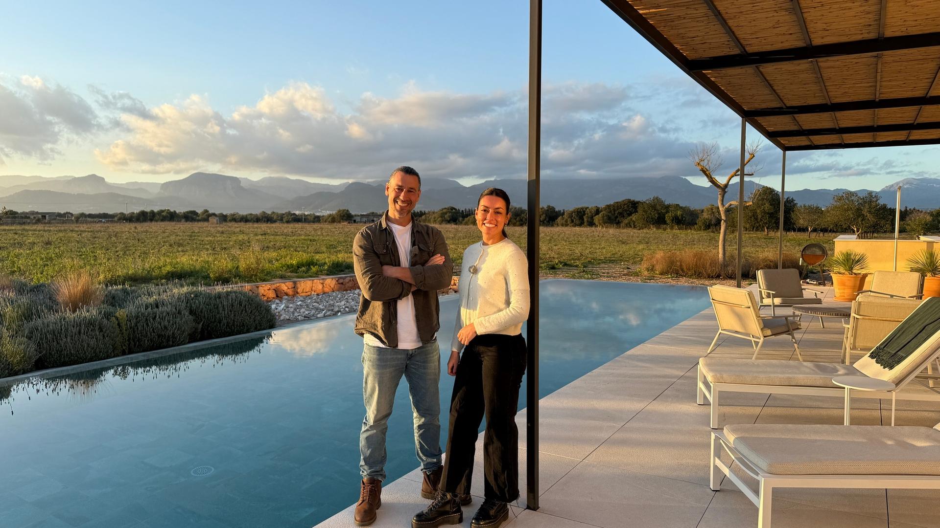 "Garden Dreams": Davit Arican und Lourdes Vázquez stehen auf einer Terrasse vor einem Pool. Davit Arican hat die Arme vor seinem Körper verschränkt. Im Hintergrund liegt das Tramuntana Gebirge.