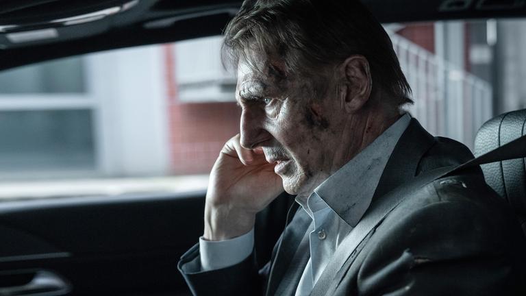 "Retribution - Vergeltung": Nahaufnahme: Matt (Liam Neeson) sitzt mit verschmutztem Gesicht und angespanntem Blick im Auto am Steuer.