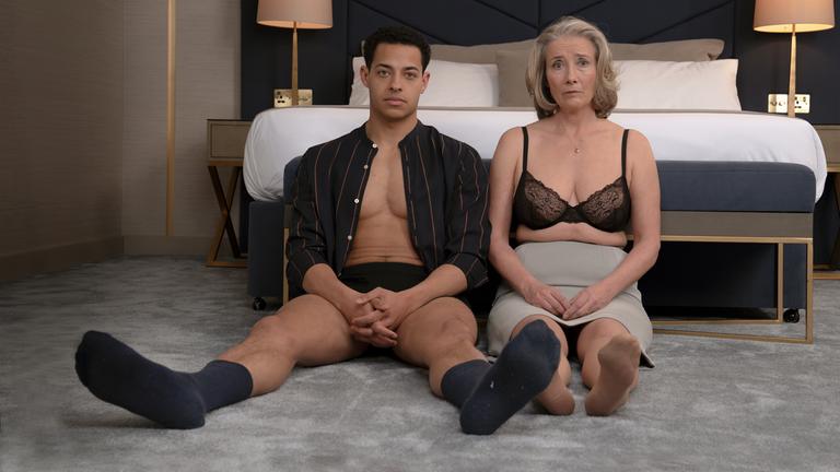 „Meine Stunden mit Leo“: Nancy (Emma Thompson) und ihr Lover Leo Grande (Daryl McCormack) sitzen mit fragendem Blick auf dem Teppichboden vor einem unbenutzten Doppelbett. Sie trägt nur noch einen Rock und dunklen BH, er ein offenes Hemd, Shorts und Socken.