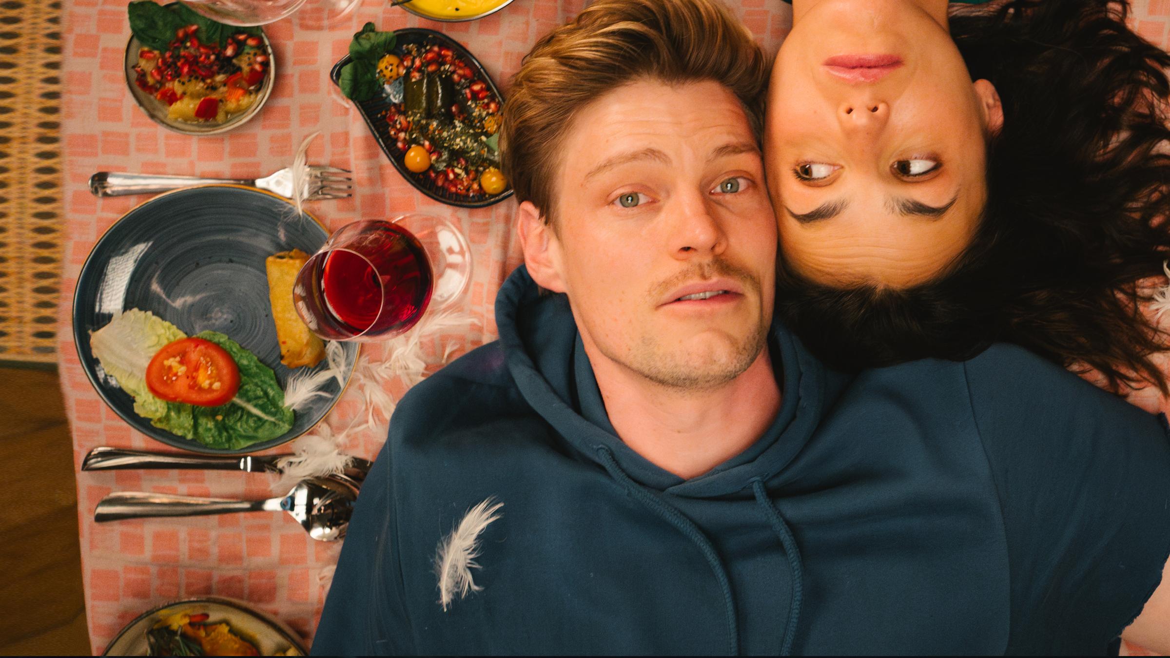 "Feste Feiern":  Knut (Helgi Schmid, re) und Karo (Lucie Heinze, li) liegen auf dem Rücken und mit den Köpfen nebeneinander auf einem gedeckten Tisch.