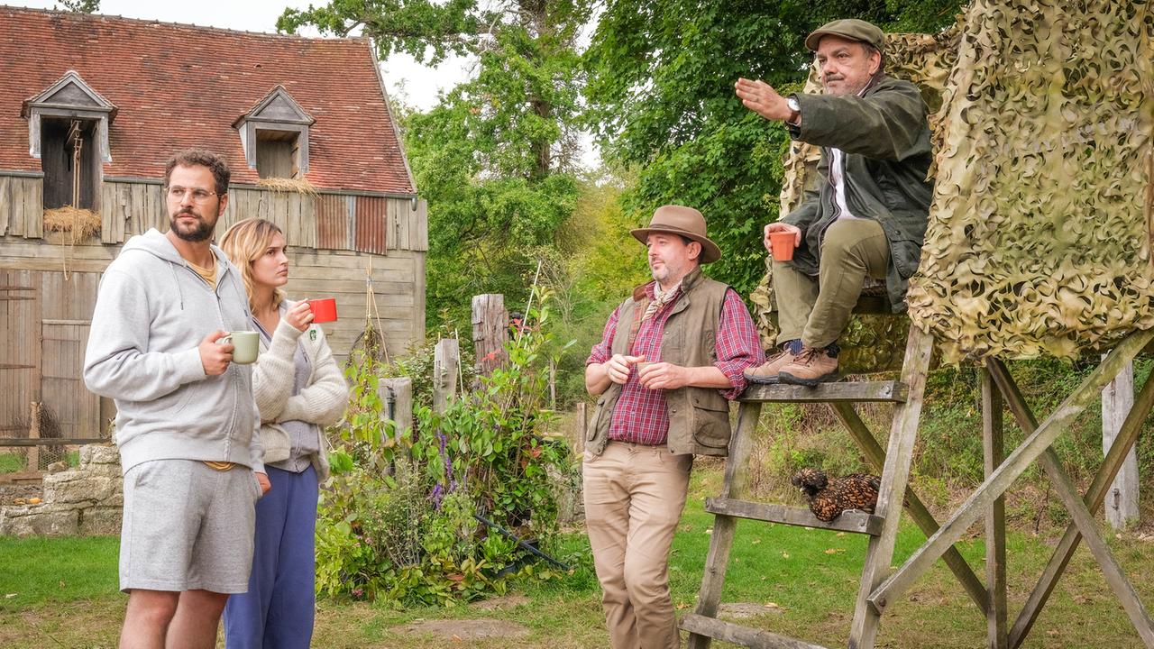 "Jagen auf französisch": Im Garten vor dem Haus: Simon (Hakim Jemili) und seine Frau Adélaϊde (Camille Lou) stehen mit Tassen in der Hand vor Bernard (Didier Bourdon), der auf dem Hochsitz Platz genommen hat und Bernards Freund Michel (Jean-François Cayrey), der an den Hochsitz angelehnt steht.