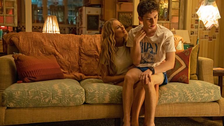 "No Hard Feelings": In Shorts und T-Shirt sitzt Percy (Andrew Barth Feldman) auf einem großen Wohnzimmersofa auf Maddies Schoß. Während Maddie (Jennifer Lawrence) ihn neugierig anschaut, weicht Percy ihrem Blick verzagt aus.