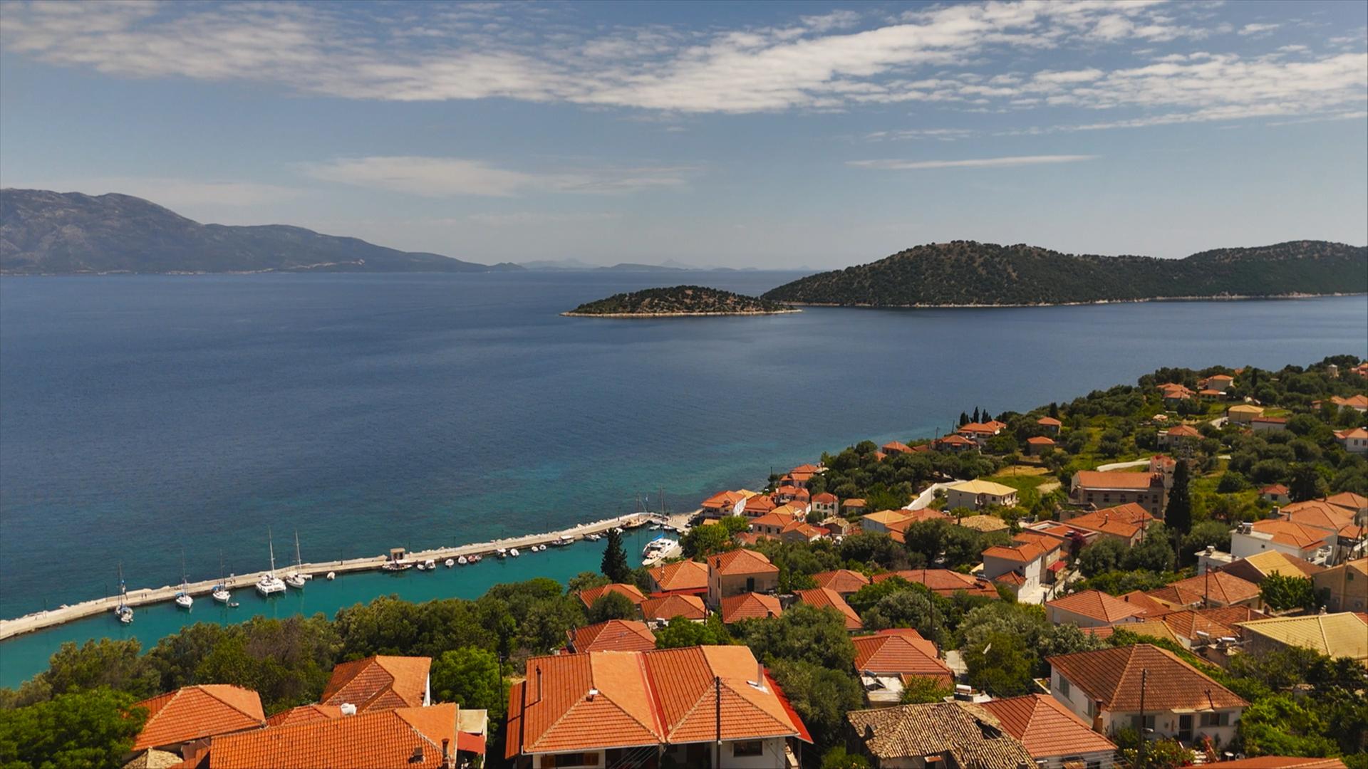 "plan b: Bewusst unterwegs - Reisen mit kleinem Budget": Landschaftspanorama: Häuser mit roten Dächern stehen am Meer, im Hintergrund liegt eine Bergkette, der Himmel ist bewölkt.