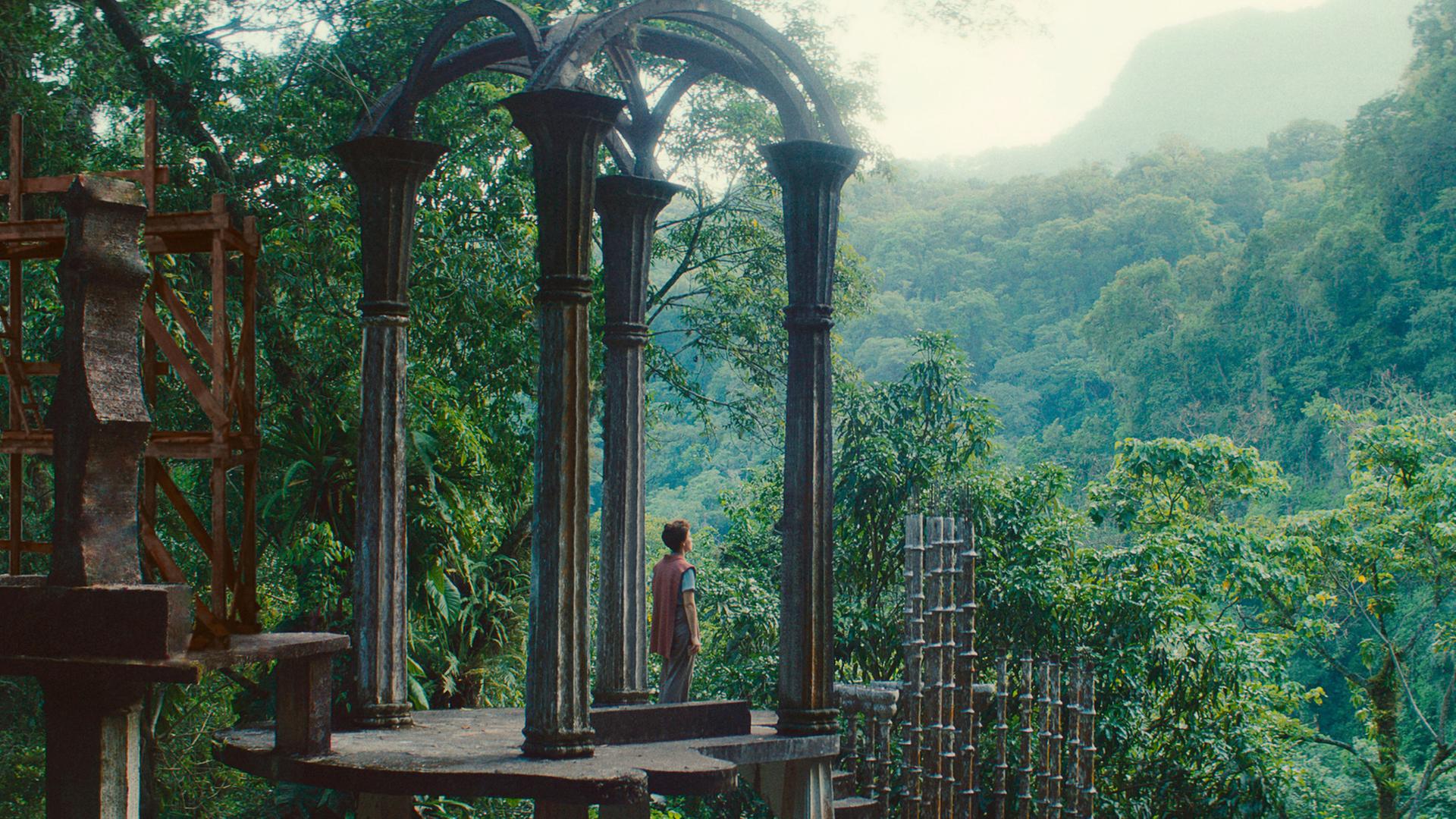 Leonora Carrington (Olivia Vinall) steht auf einer Plattform im Dschungel und blickt in die Natur.
