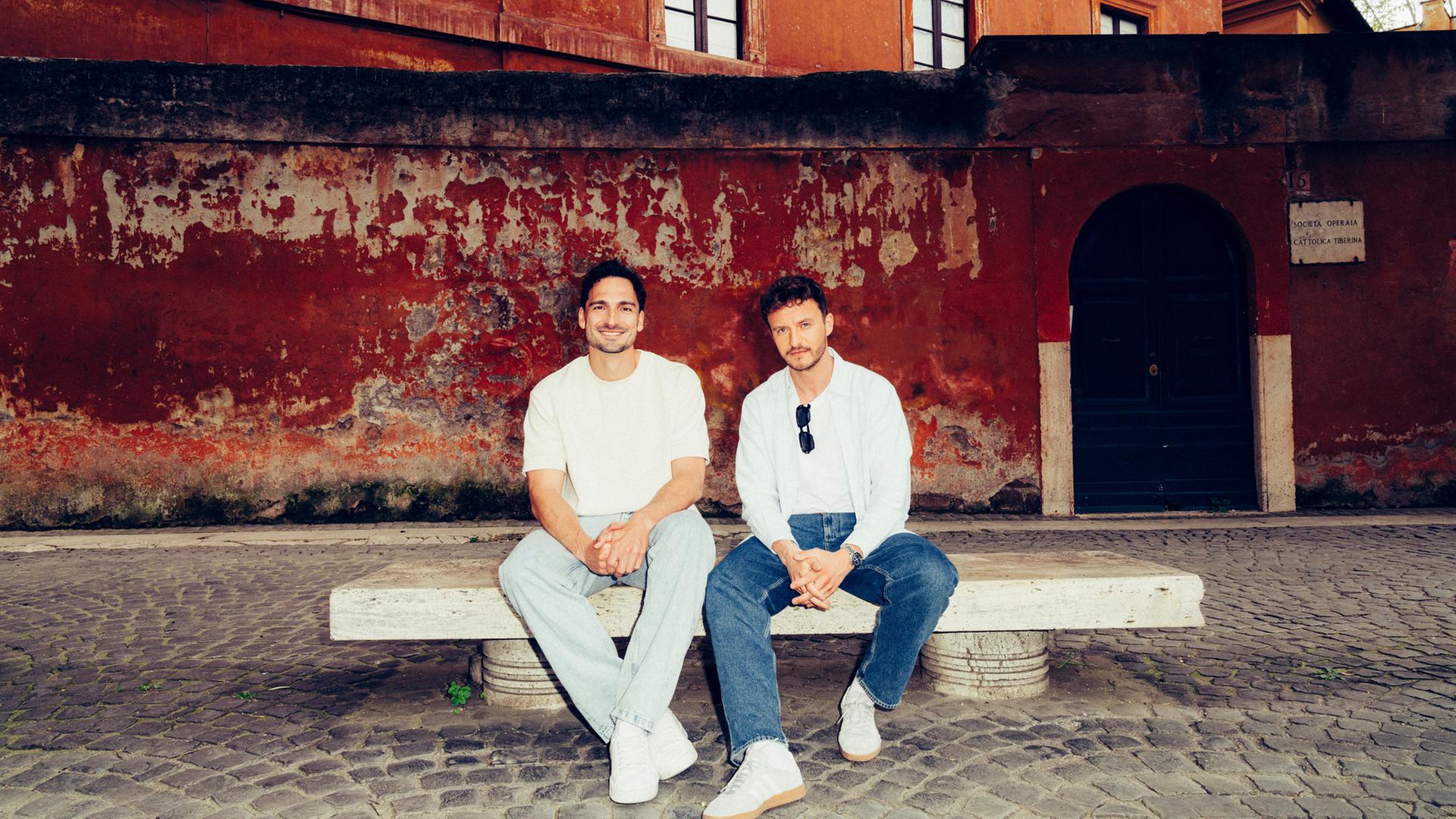 "Hummels - La Finale. Mit Tommi Schmitt": Mats Hummels und Tommi Schmitt sitzen auf einer Bank in Rom. Sie schauen in die Kamera.