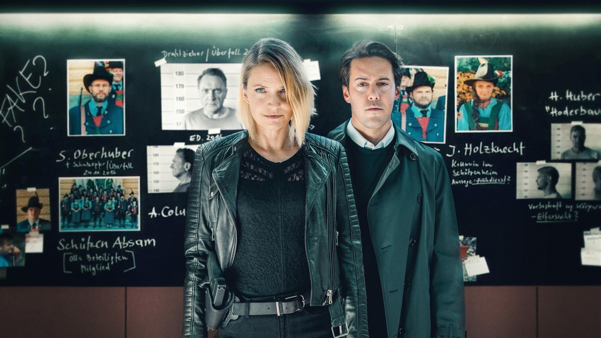 "Der Tote in der Schlucht": Lisa Kuen (Patricia Aulitzky) und Alexander Yüsüf-Demir (Dominik Raneburger) stehen vor einer Tafel mit Fotos und handschriftlichen Notizen. Beide schauen ernst in die Kamera. Die Tafel enthält Bilder von mehreren Personen sowie Diagramme und Textfragmente.