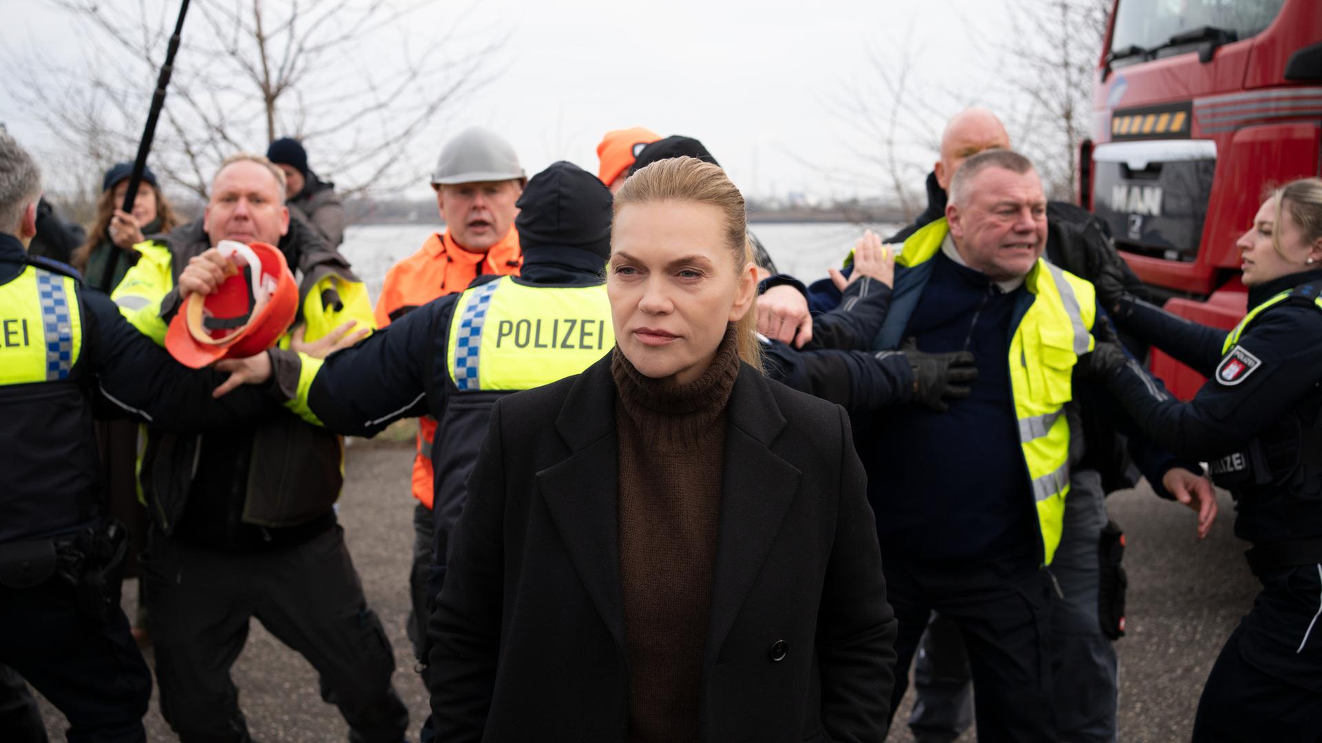 "Helen Dorn - Schuld und Sühne": Helen Dorn (Anna Loos) steht draußen. Im Hintergrund halten Polizisten die Demonstranten auf.