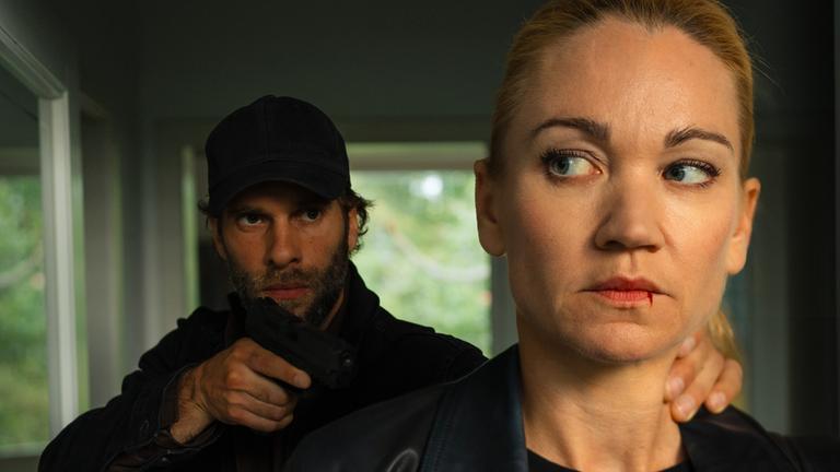 "Sarah Kohr - Im Schatten": Sarah Kohr (Lisa Maria Potthoff) steht mit verängstigtem Blick und blutender Wunde an ihrer Lippe vor Hannes Kosinski (Mathis Landwehr), der sie an den Hals fasst und mit einer Waffe bedroht.
