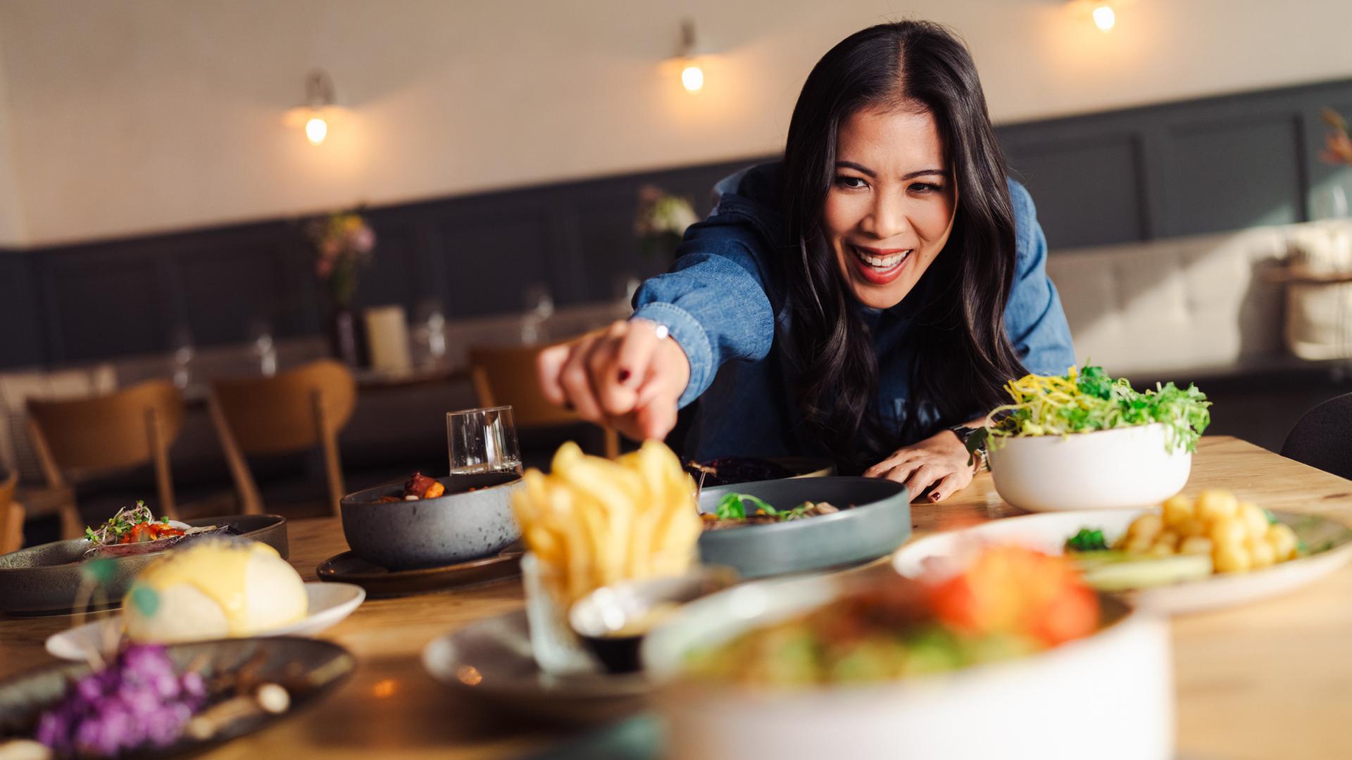 "Chemie des Kochens - Wasser": Dr. Mai Thi Nguyen-Kim greift über den mit verschiedenen Speisen gedeckten Tisch und versucht sich mit ausgestrecktem Arm Pommes Frites zu greifen.
