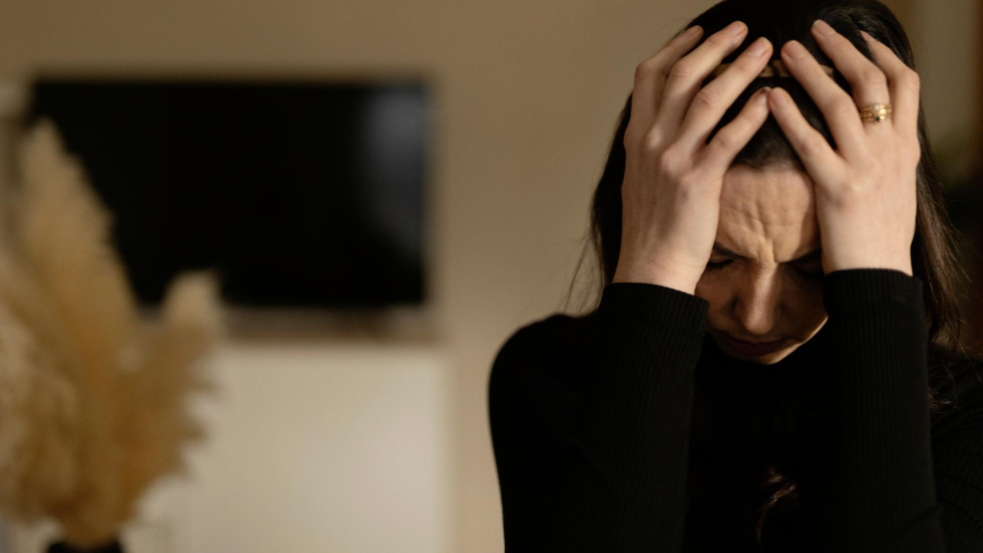 "Kampf im Kopf: Leben mit Depression": Michelle ist in einem Innenraum und hat den Kopf gesenkt. Sie hält diesen mit beiden Händen.