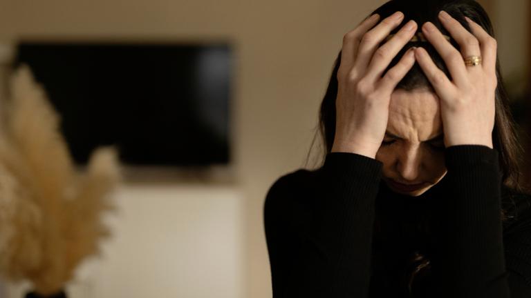 "Kampf im Kopf: Leben mit Depression": Michelle ist in einem Innenraum und hat den Kopf gesenkt. Sie hält diesen mit beiden Händen.