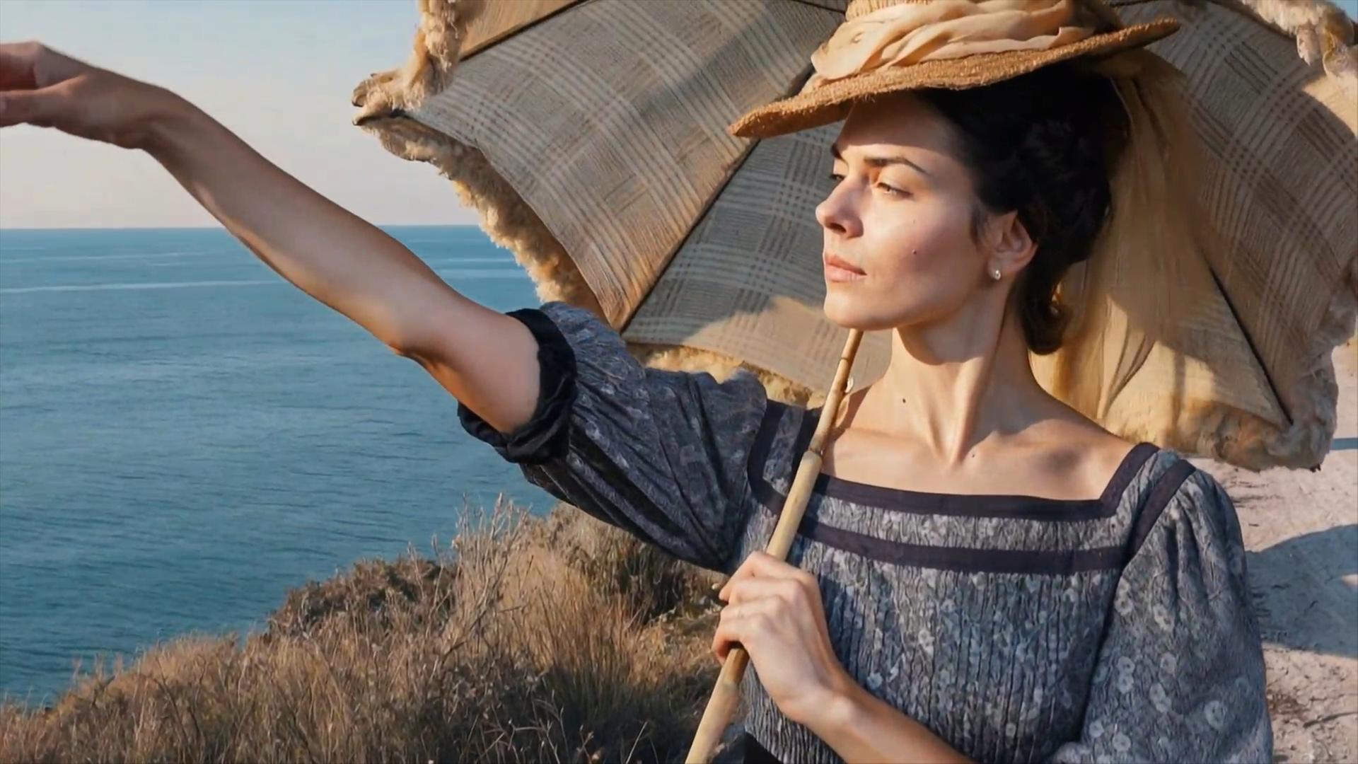 "Terra X History: Weltberühmt und depressiv - Von Sisi bis Adenauer": KI-generierte Spielszene: Kaiserin Sisi steht am Meeresufer. Sie trägt ein geblümtes Kleid und hat einen Arm nach vorne ausgestreckt. In der anderen Hand hält sie einen Sonnenschirm.