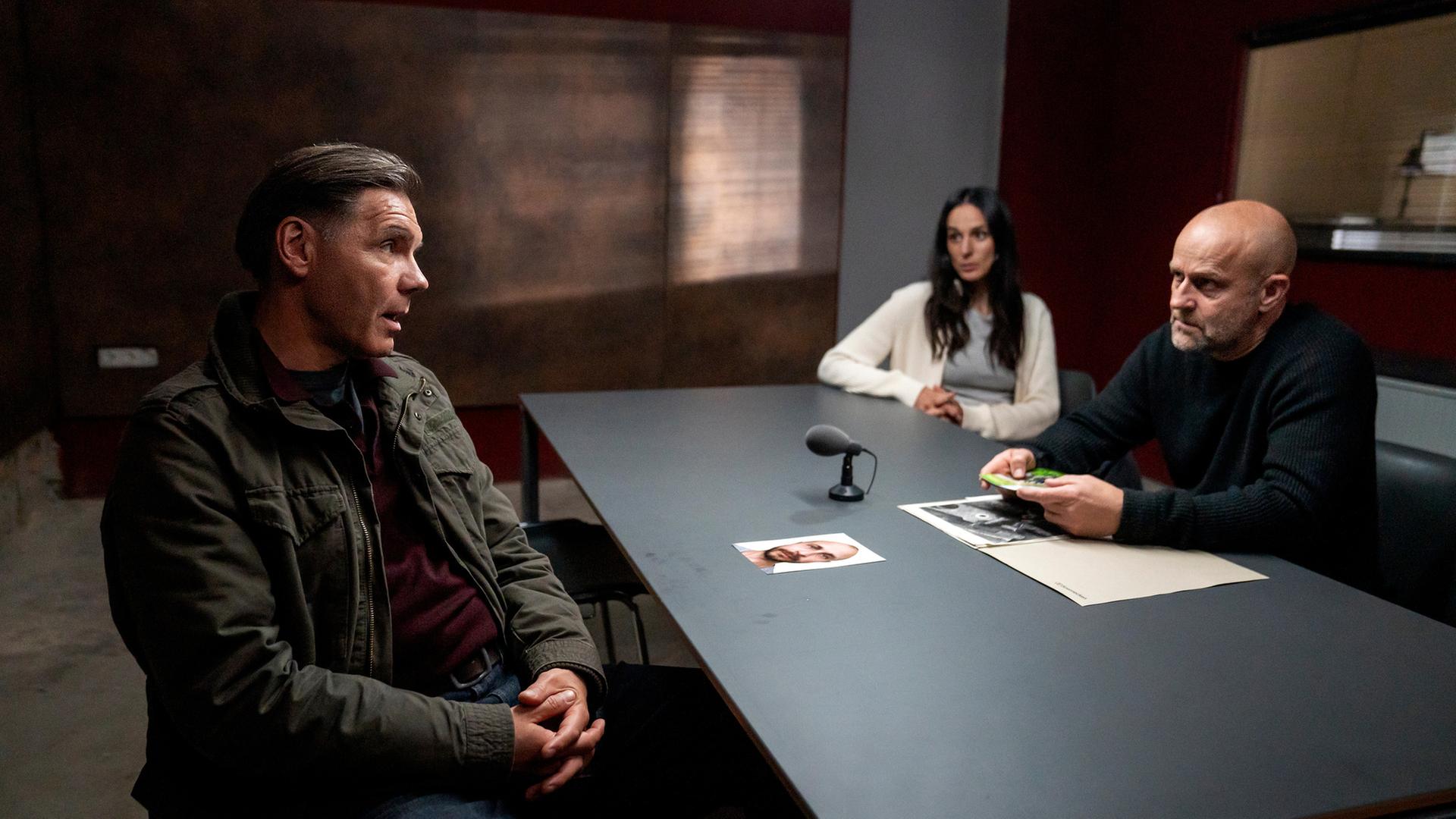  "Jenseits der Spree - Im Land der toten Träume": Wolfgang Sparla (Max Hopp) sitzt Mavi Neumann (Aybi Era) und Robert Heffler (Jürgen Vogel) im Verhörraum an einem Tisch gegenüber. Auf dem Tisch steht ein Mikrofon. Robert hat eine aufgeschlagene Akte vor sich liegen.