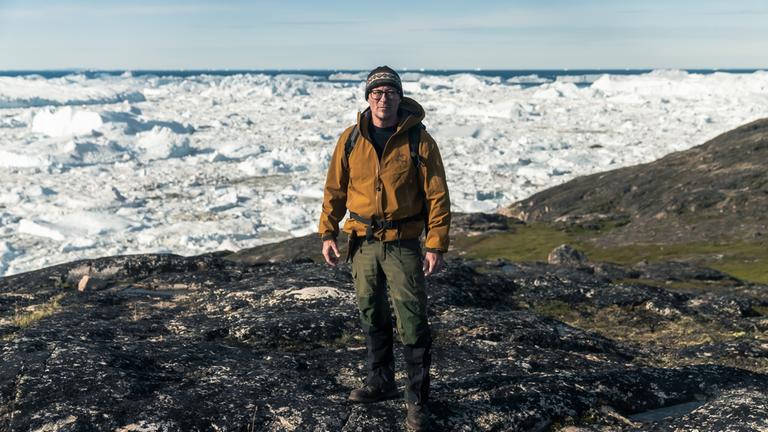 "Terra X: Vor der Eiszeit - Jagd nach dem ältesten Erbgut der Welt": Eske Willerslev ist Evolutionsgenetiker und steht bei einer Expedition auf einer eisfreien Fläche, hinter ihm erstreckt sich eine schnee- und eisbedeckte Landschaft.