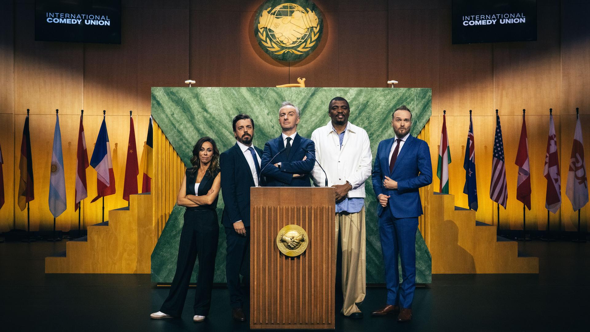 Bildbeschreibung: "ZDF Magazin Royale präsentiert: International Comedy Union": Filomena Cautela, Anders Helenius, Jan Böhmermann, Loyiso Gola und Arjen Lubach posieren gemeinsam am Rednerpult der "International Comedy Union".