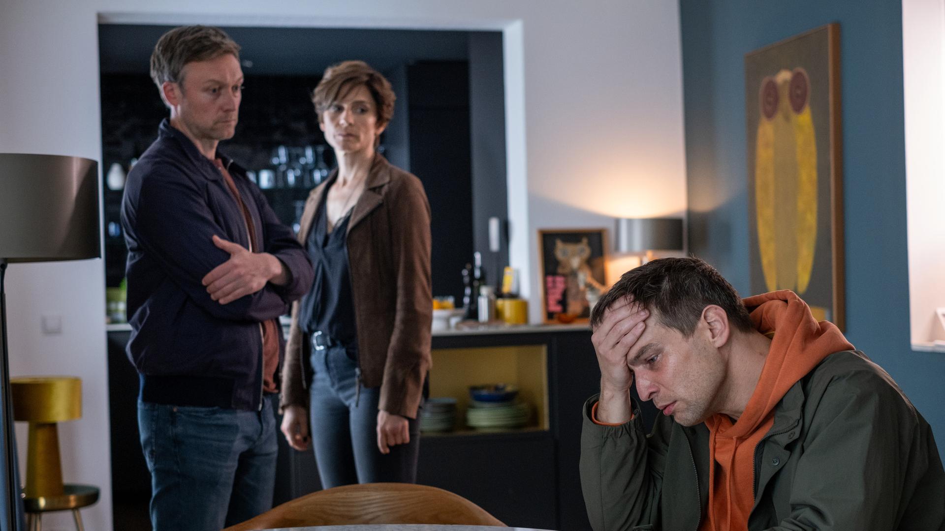 "In Wahrheit - Für immer Dein": In einem Wohnraum: Moritz Brück (Robert Finster) sitzt an einem Tisch und stützt seinen Kopf mit der Hand. Er blickt bedrückt nach unten. Im Hintergrund stehen Freddy Breyer (Robin Sondermann) und Judith Mohn (Christina Hecke) und schauen besorgt zu ihm.