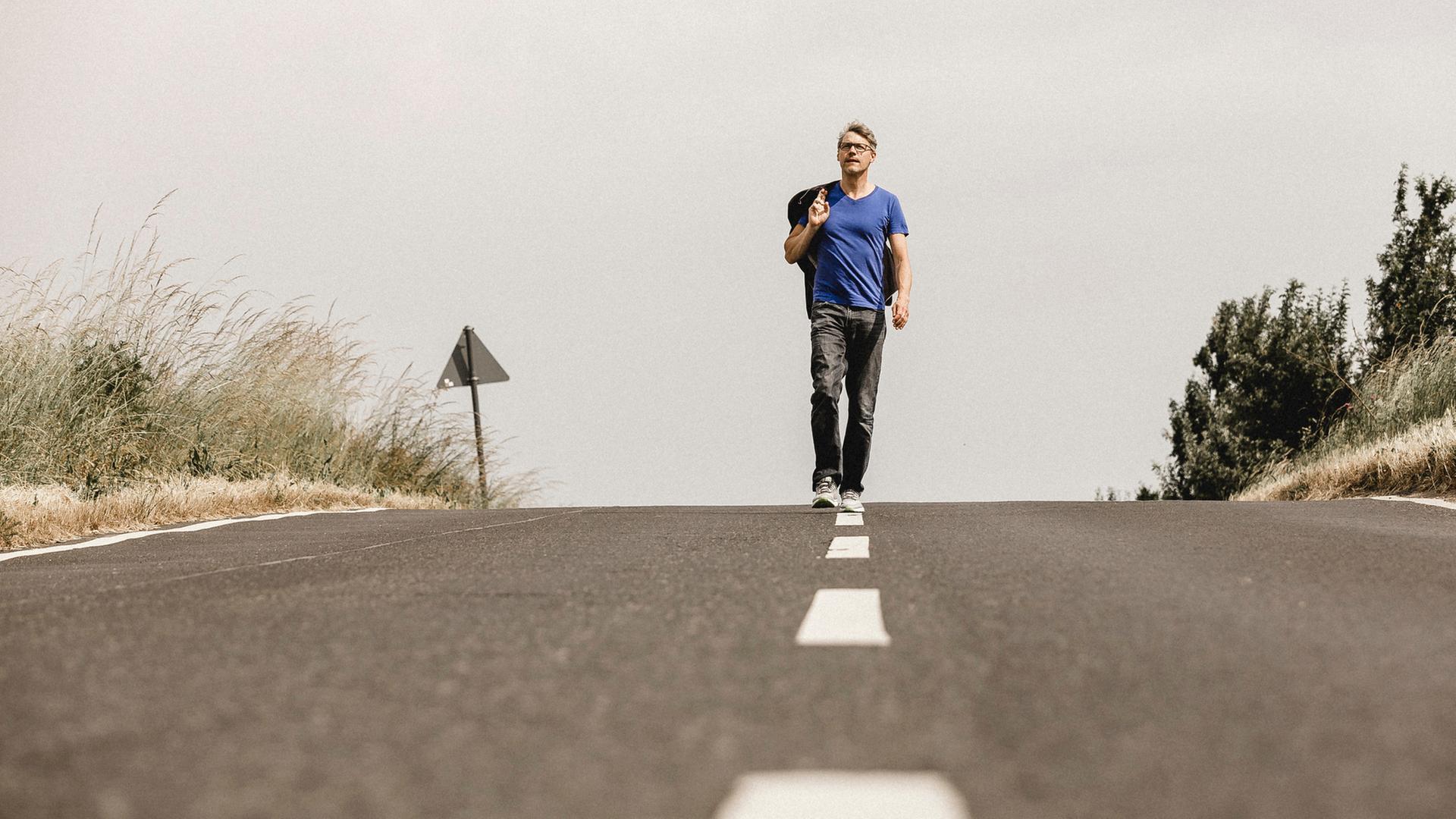 "Christoph Sieber: Weitermachen!":  Christoph Sieber läuft auf der Mittellinie einer Landstraße.