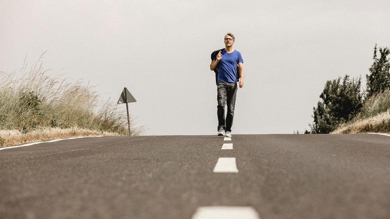 "Christoph Sieber: Weitermachen!":  Christoph Sieber läuft auf der Mittellinie einer Landstraße.