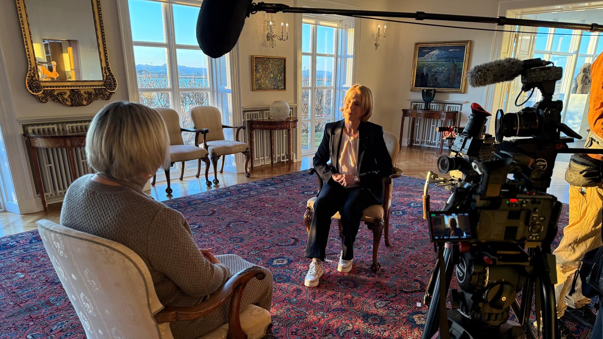 "auslandsjournal - die doku: So geht Frieden! - Wie Waffen niederlegen?": Katrin Eigendorf und die isländischen Präsidentin Halla Tómasdóttir sitzen sich während eines Interviews in einem großen, repräsentativen Raum gegenüber. An der Seite steht eine Kamera, oben befindet sich eine Tonangel mit Mikrofon.