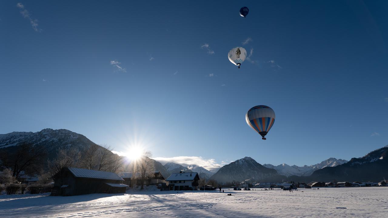 "Terra X: Spektakuläre Meilensteine der Ballonfahrt": Drei Heißluftballons starten in den blauen, wolkenfreien Himmel über einem Alpenpanorama über dem gerade die Sonne aufgeht.